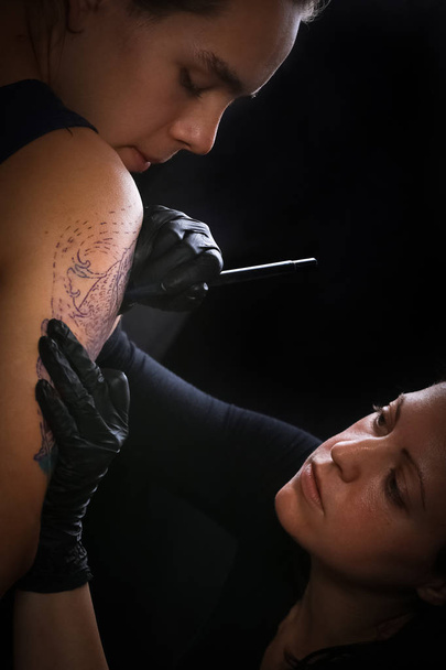 Женщина-татуировщица делает татуировку на руке мужчины
 - Фото, изображение