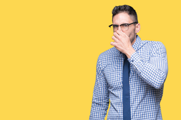 Jeune homme d'affaires portant des lunettes sur fond isolé sentant quelque chose de puant et dégoûtant, odeur intolérable, retenant souffle avec les doigts sur le nez. Concept de mauvaises odeurs
. - Photo, image