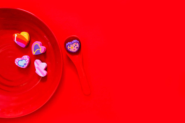 Valentine is Day Colorful Heart on a Red Plate and Spoon for Love Concept. Flat Eraser in Shape of a Heart with Sweet and Romantic. Different Rubber Heart Symbol Isolated on Red Paper Background. - 写真・画像