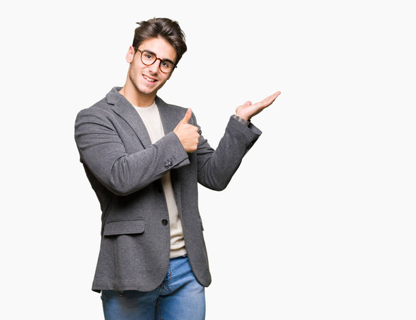 Young business man wearing glasses over isolated background Showing palm hand and doing ok gesture with thumbs up, smiling happy and cheerful - Фото, зображення