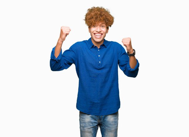 Young handsome elegant man with afro hair very happy and excited doing winner gesture with arms raised, smiling and screaming for success. Celebration concept. - Photo, image