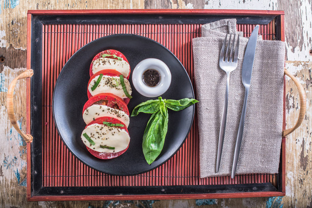 Tomates con queso y albahaca en plato con salsa sobre mesa de madera
 - Foto, Imagen