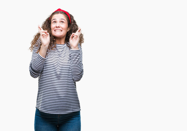 Mooie brunette krullend haar jong meisje dragen strepen trui over geïsoleerde achtergrond glimlachend kruising vingers met de ogen gesloten en hoop. Geluk en bijgelovig concept. - Foto, afbeelding