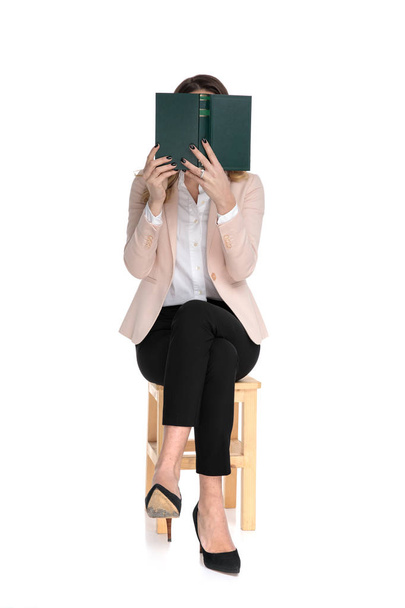 captivated smart casual woman reading a book while sitting on wooden chair, full body picture - Photo, Image