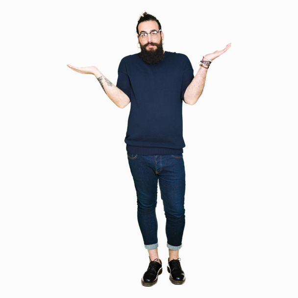 Jonge hipster man met lange haren en baard dragen brillen Smiling tonen dat beide handen open palmen, presentatie en reclame vergelijking en evenwicht - Foto, afbeelding
