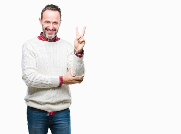 Keski-ikäinen hoary vanhempi mies yllään talvi villapaita yli eristetty tausta hymyillen onnellinen kasvot silmää kameran tekemässä voitto merkki. Numero kaksi.
. - Valokuva, kuva