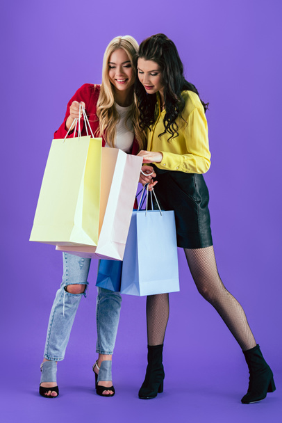 Curious girls looking in shopping bags on purple background - Fotó, kép