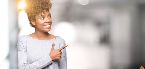 Όμορφη νεαρή αφρικανική αμερικανική γυναίκα πέρα από το απομονωμένο υπόβαθρο χαρούμενα με ένα χαμόγελο του προσώπου δείχνει με το χέρι και δάχτυλο μέχρι την πλευρά με ευτυχισμένο και φυσική έκφραση στο πρόσωπό - Φωτογραφία, εικόνα