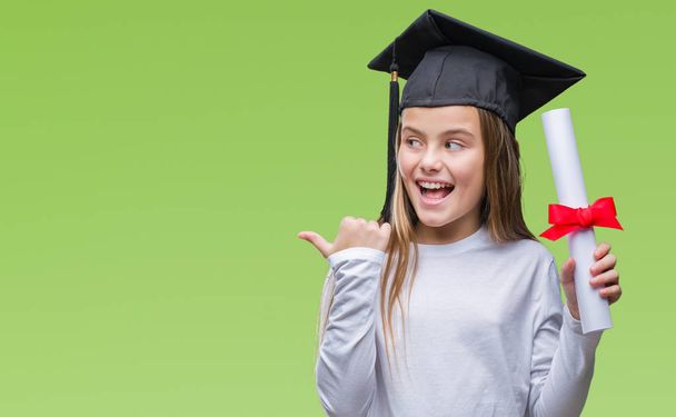 Молода красива дівчина в шапці випускника тримає ступінь над ізольованим тлом, вказуючи і показуючи з великим пальцем в сторону з щасливим обличчям посміхаючись
 - Фото, зображення