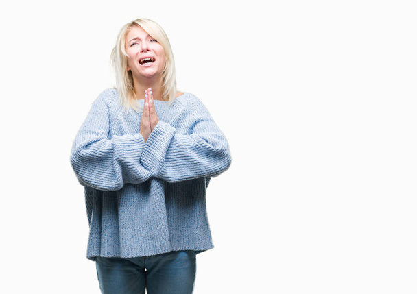 Young beautiful blonde woman wearing winter sweater over isolated background begging and praying with hands together with hope expression on face very emotional and worried. Asking for forgiveness. Religion concept. - Photo, Image