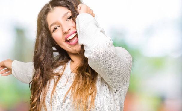 Mujer hermosa joven vistiendo suéter blanco Bailando feliz y alegre, sonriente moviéndose casual y confiado escuchando música
 - Foto, imagen