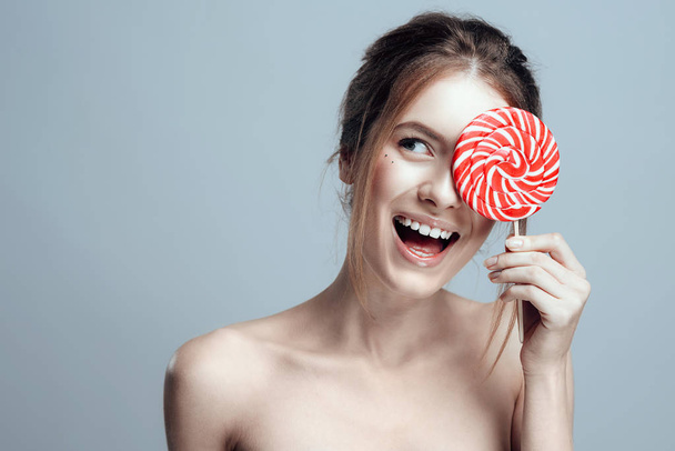 Close-up photo of a beautiful girl with a lollipop. She has clean and even skin, fair hair. - Фото, зображення