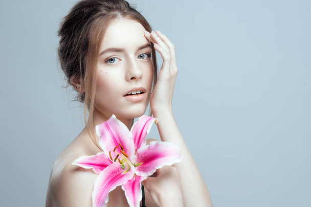 Close-up photo of a beautiful girl with a lily flower. She has clean and even skin, fair hair. - Foto, Bild