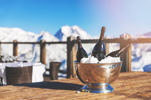 κουβά με μπουκάλια σαμπάνιας σε εστιατόριο τραπέζι χιονισμένο βουνό φόντο - Φωτογραφία, εικόνα
