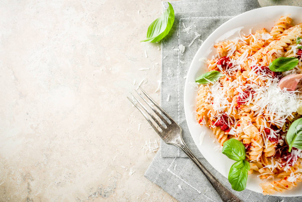 Italian food, fusilli pasta with  tomato sauce, grated parmesan cheese and basil, light stone table copy space top view - Foto, Imagen