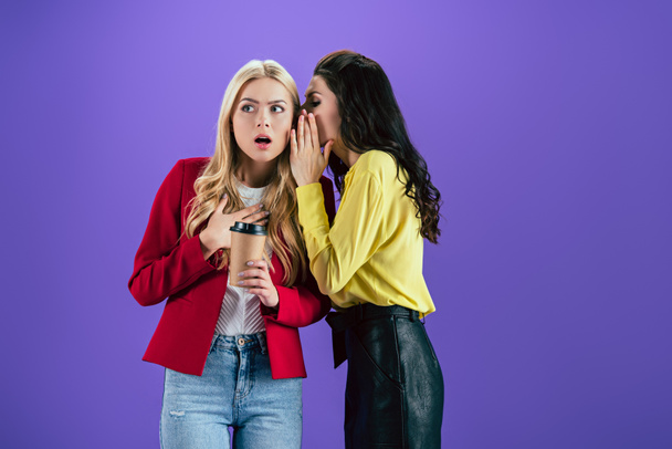 brünettes Mädchen wünscht Geheimnis im Ohr eines Freundes auf lila Hintergrund - Foto, Bild