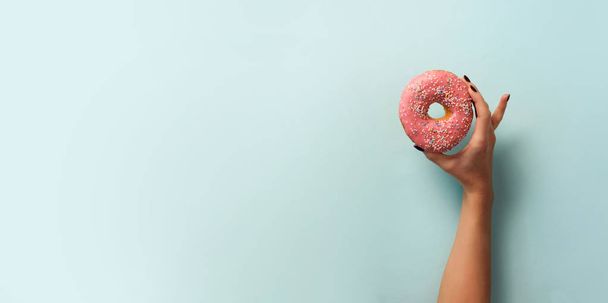 Female hand holding sweet donut over blue background. Top view, flat lay. Weight lost, sport, fitness concept. Banner with copy space - Φωτογραφία, εικόνα