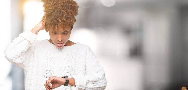 Linda jovem afro-americana vestindo camisola de inverno sobre fundo isolado Olhando para o relógio tempo preocupado, com medo de se atrasar
 - Foto, Imagem