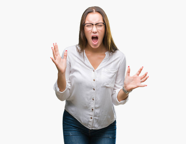 Young caucasian beautiful business woman wearing glasses over isolated background crazy and mad shouting and yelling with aggressive expression and arms raised. Frustration concept. - Φωτογραφία, εικόνα