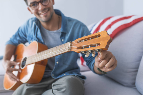 Portrait of young man sitting on sofa and playing guitar - Foto, Imagem