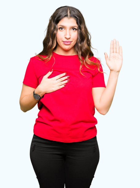junge schöne Frau in lässigem T-Shirt, die mit der Hand auf der Brust und offener Handfläche schwört und einen Treueschwur ablegt - Foto, Bild