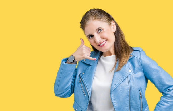 Beautiful middle age mature woman wearing fashion leather jacket over isolated background smiling doing phone gesture with hand and fingers like talking on the telephone. Communicating concepts. - Photo, Image