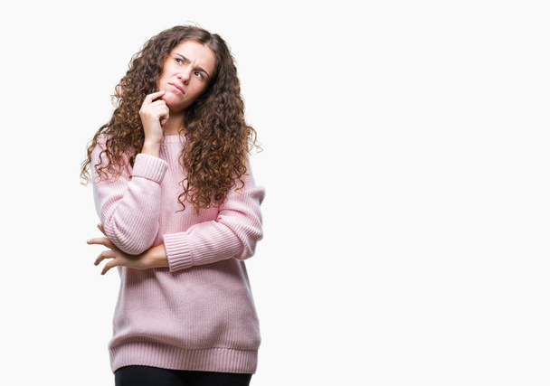 Linda morena cabelo encaracolado menina vestindo suéter de inverno rosa sobre fundo isolado com a mão no queixo pensando em questão, expressão pensativa. Sorrindo com cara atenciosa. Conceito de dúvida
. - Foto, Imagem