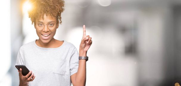 Νεαρός αφρικανική αμερικανική γυναίκα χρησιμοποιώντας smartphone μέσω απομονωμένη φόντο έκπληξη με μια ιδέα ή ένα ερώτημα που δείχνει δάχτυλο με χαρούμενο πρόσωπο, αριθμός - Φωτογραφία, εικόνα