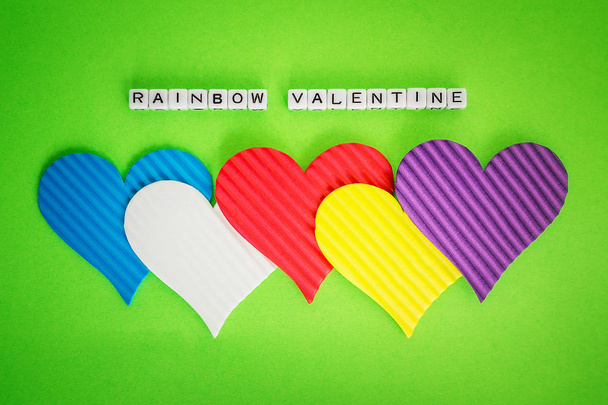 Five multicolored valentine hearts and the inscription Rainbow Valentine made of white alfphabet cubeson a green background. Concept of LGBT, love and valentine's day. Flat lay, top view. - Zdjęcie, obraz
