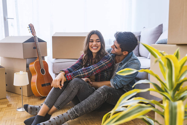 Young couple sitting on floor in new home with cardboard boxes  - Foto, imagen