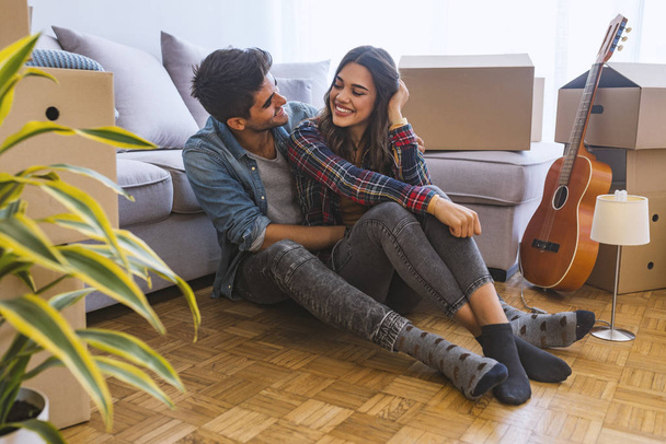 Young couple sitting on floor in new home with cardboard boxes  - Fotoğraf, Görsel