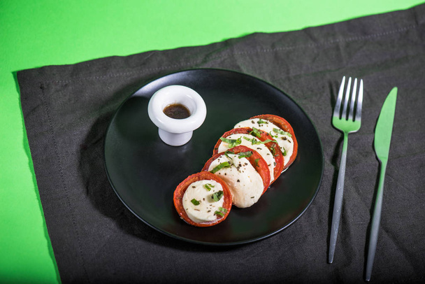 Snack with tomatoes and cheese on black plate with sauce - Foto, Imagen