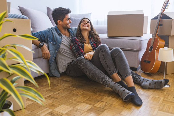 Young couple sitting on floor in new home with cardboard boxes  - Фото, зображення