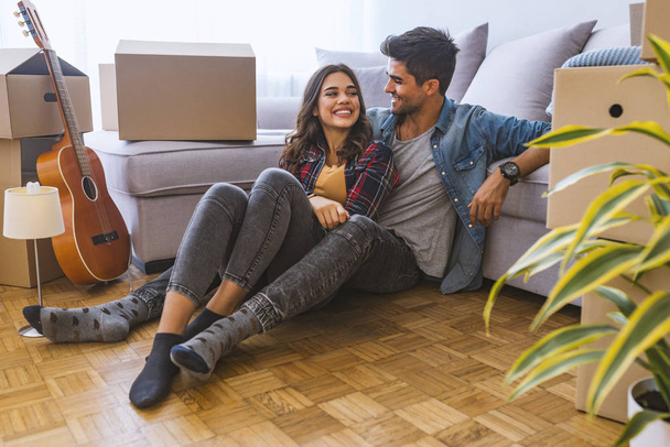 Young couple sitting on floor in new home with cardboard boxes  - Fotografie, Obrázek