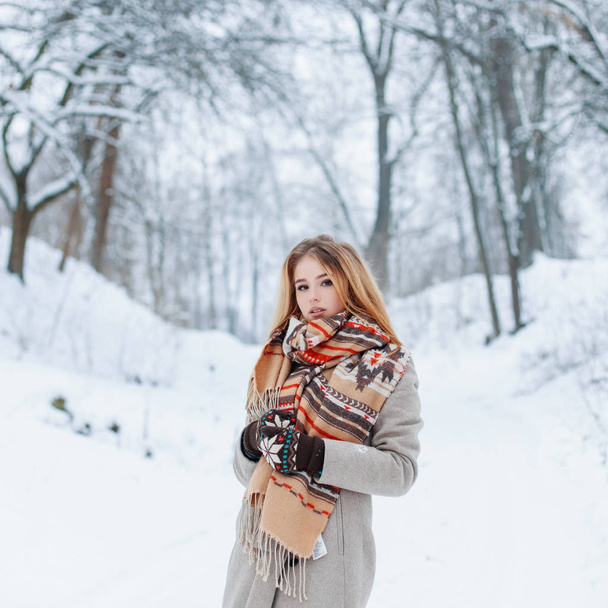 Приваблива молода дівчина стильно з вовняним теплим шарфом у модному сірому зимовому пальто в вінтажних в'язаних рукавицях проводить вихідні в парку. Чарівна стильна дівчина
. - Фото, зображення