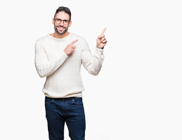 Young handsome man wearing glasses over isolated background smiling and looking at the camera pointing with two hands and fingers to the side. - Photo, Image