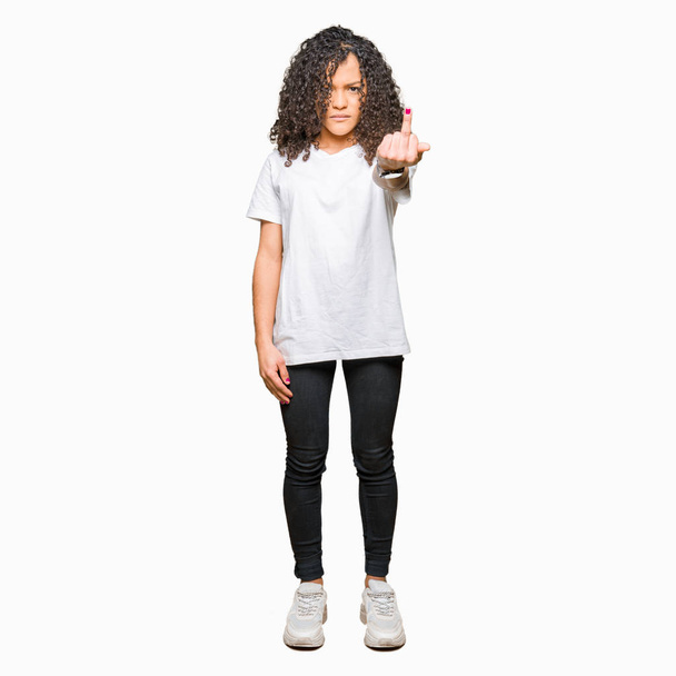 Young beautiful woman with curly hair wearing white t-shirt Showing middle finger, impolite and rude fuck off expression - Foto, Imagen