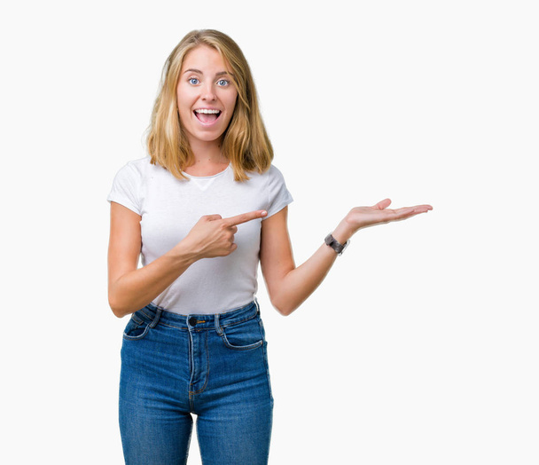 Mulher bonita vestindo casual t-shirt branca sobre fundo isolado espantado e sorrindo para a câmera ao apresentar com a mão e apontando com o dedo
. - Foto, Imagem