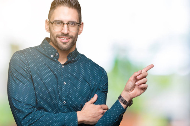 Young handsome business man wearing glasses over isolated background with a big smile on face, pointing with hand and finger to the side looking at the camera. - Photo, Image