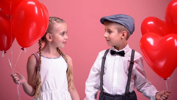 Boy and girl holding red heart balloons and looking at each other, first love - Φωτογραφία, εικόνα