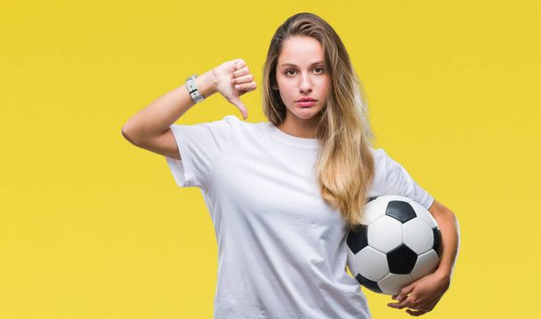 Młody piękny blond kobieta trzymając piłki nożnej na na białym tle z gniewną twarz, minus Wyświetlono niechęć z kciuk w dół, odrzucenie koncepcji - Zdjęcie, obraz