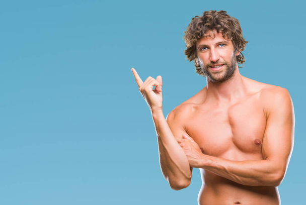 Knappe Spaanse model man sexy en shirtless over geïsoleerde achtergrond met een grote glimlach op het gezicht, met de hand en de vinger te wijzen naar de kant te kijken naar de camera. - Foto, afbeelding
