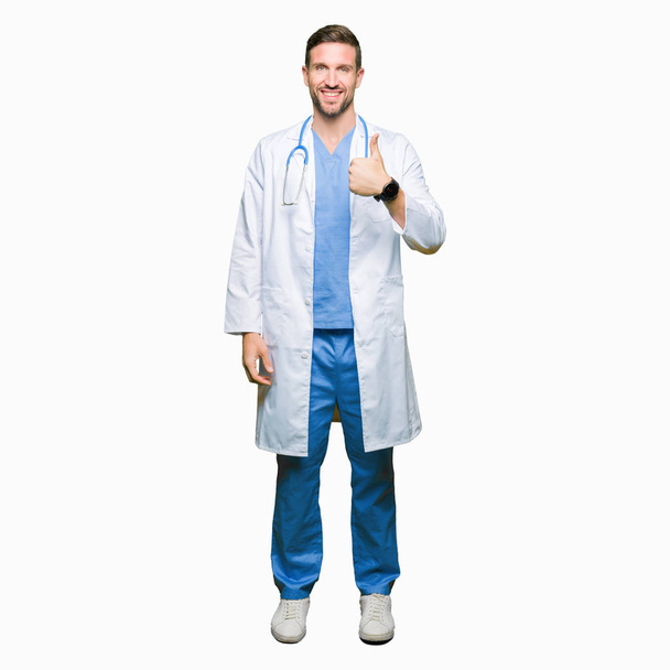 Csinos orvos férfi orvosi egységes visel, több mint boldog remek gesztus kézzel elszigetelt háttérben. Nézi a kamera mutatja a siker kifejezés jóváhagyásáról. - Fotó, kép