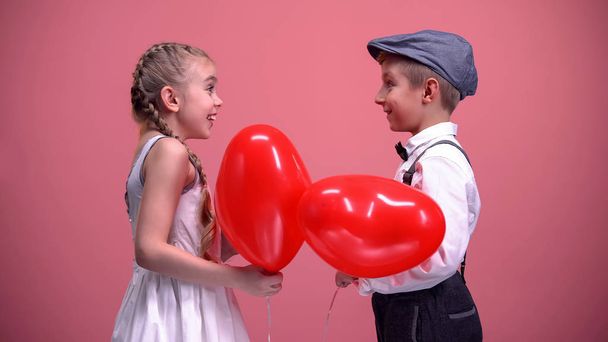 Couple of cute kids exchanging red heart-shaped balloons, Valentines day gift - Fotografie, Obrázek
