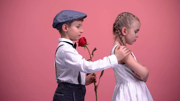 Маленький милий хлопчик з червоною трояндою вибачився перед ображеною дівчиною, перше кохання
 - Фото, зображення