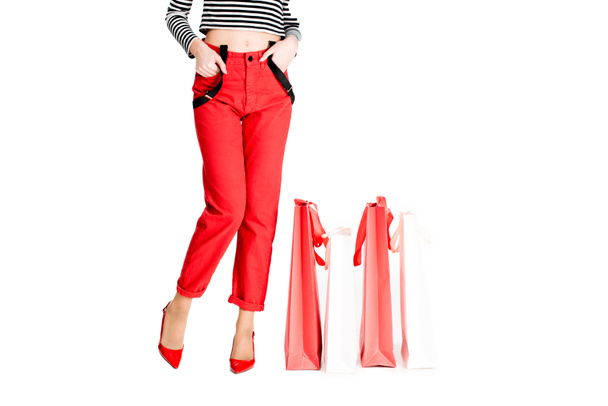 cropped view of woman standing with hands in pockets near red shopping bags isolated on white  - Фото, изображение