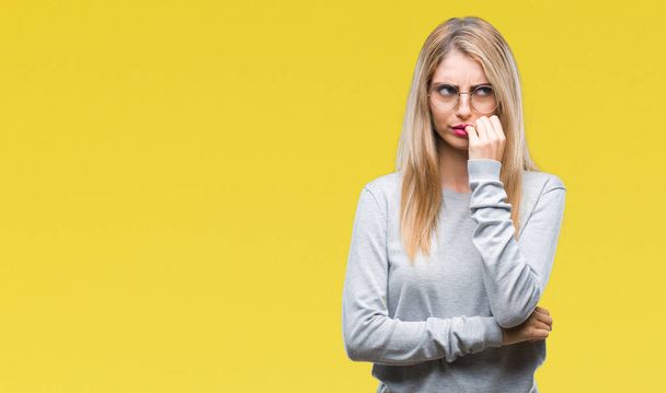 Young beautiful blonde woman wearing glasses over isolated background looking stressed and nervous with hands on mouth biting nails. Anxiety problem. - Photo, Image