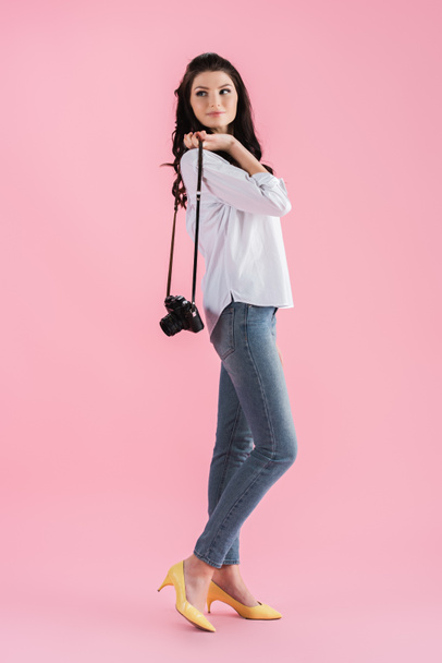 verträumtes Mädchen hält Digitalkamera in der Hand und schaut auf rosa Hintergrund weg - Foto, Bild