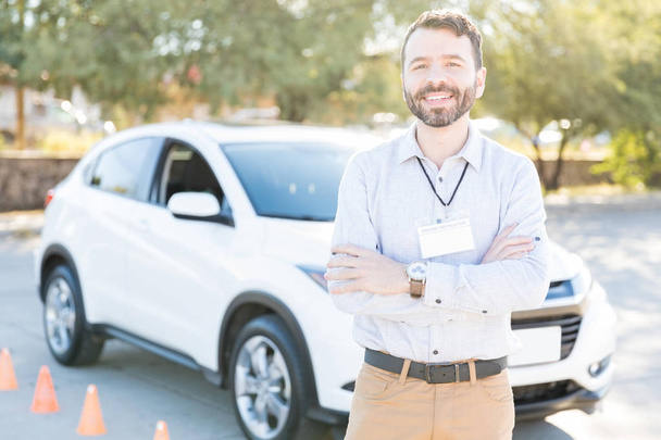 Auto driving instructor standing with arms crossed against car on street - Photo, Image