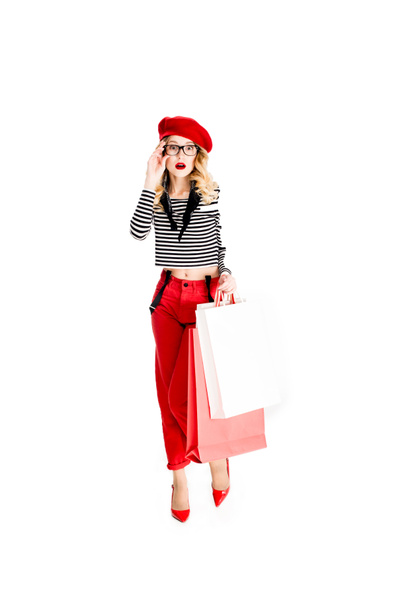 surprised woman in glasses and red beret holding shopping bags isolated on white  - Photo, Image